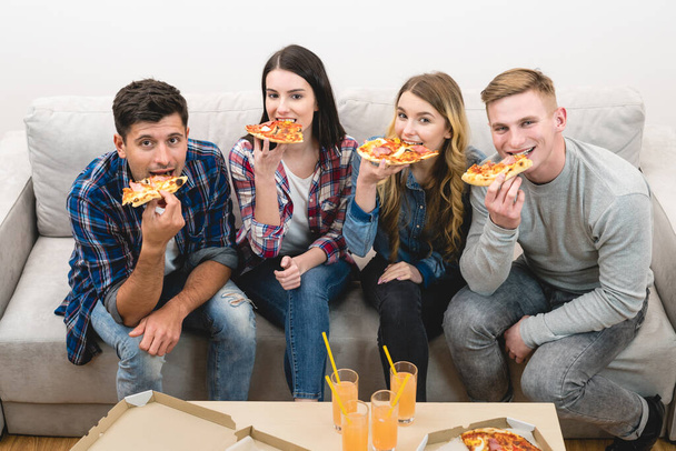 Neljä onnellista ihmistä sohvalla syömässä pizzaa. - Valokuva, kuva