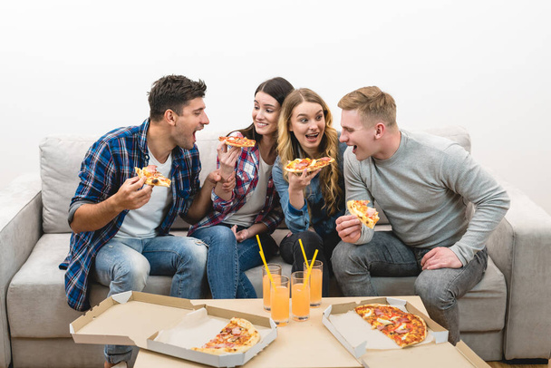 Les quatre personnes heureuses sur le canapé mangent de la pizza sur le fond blanc
 - Photo, image