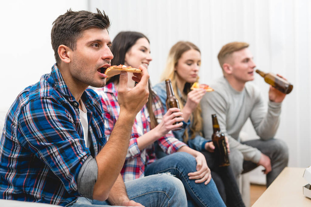 Les quatre amis sur le canapé mangent une pizza et boivent une bière sur le fond blanc
 - Photo, image