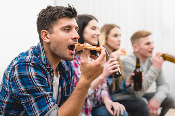 Τα τέσσερα άτομα στον καναπέ τρώνε πίτσα και πίνουν μπύρα στο λευκό φόντο. - Φωτογραφία, εικόνα