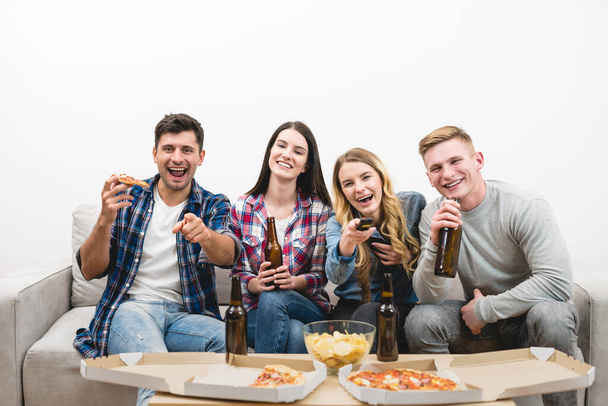 A négy boldog ember tévét néz pizzával és sörrel a fehér háttéren. - Fotó, kép