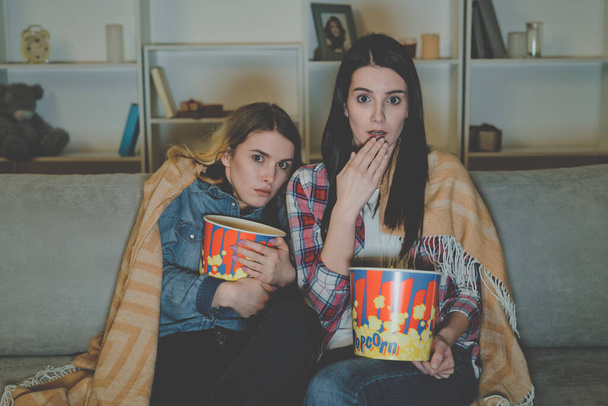 Las dos mujeres con palomitas de maíz ven una película de terror en el sofá
 - Foto, imagen