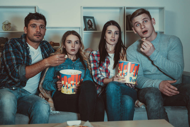 De vier vrienden met een popcorn kijken naar een horrorfilm op de bank - Foto, afbeelding