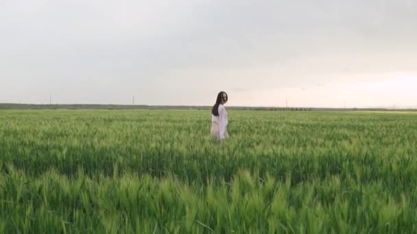 young, caucasian girl with black hair in a white shirt and skirt walks on a wheat field at sunset and feels happy - Footage, Video