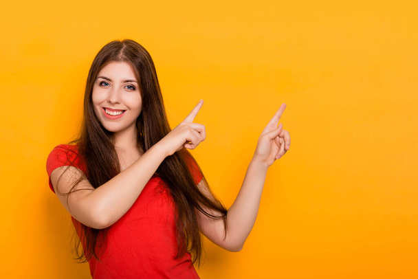 Eine junge, schöne Frau lächelt und zeigt mit dem Finger zur Seite. Studiofoto auf gelbem Hintergrund. - Foto, Bild