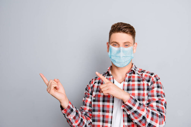 Cheerful young man pointing away wear medical safety mask on face showing data, stop pandemic corona virus prevention protection concept 2020 covid19 - Foto, Imagen