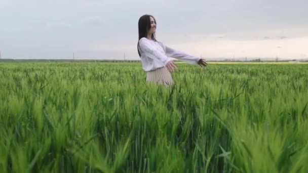 piękna dziewczyna z czarnymi włosami w białej koszuli i spódnicy spada na pole pszenicy o zachodzie słońca, - Materiał filmowy, wideo