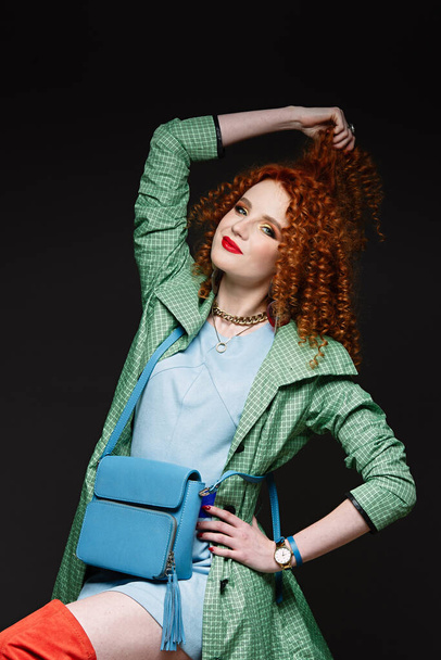 red-haired girl, curly hair, holds hands on her head, pulls her hand with her hair, bright clothes, red lipstick, head to the side, white skin, stylish clothes - Foto, Bild