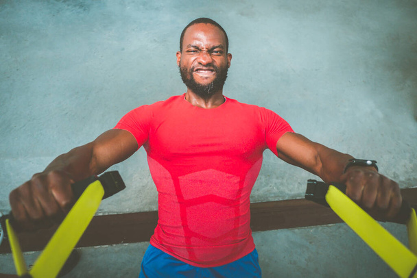 Mladý černý osobní trenér trénink ramena s trx fitness řemínky v tělocvičně - Atraktivní afro Američan dělá crossfit kliky s trx fitness řemínky v tělocvičně studio - Fotografie, Obrázek