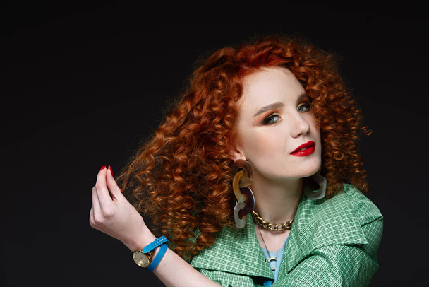 portert of a girl with curly red hair, fair skin, a green cloak, holds her hands in her arms, pulls a lock of hair to the side, red lipstick - Fotó, kép