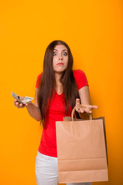 Una mujer joven y atractiva con dinero y paquetes en sus manos, ve una pérdida en el dinero restante después de comprar
. - Foto, imagen