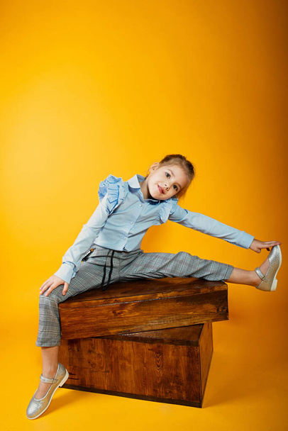 little girl sits on wooden boxes and lifted her leg to the side - Valokuva, kuva