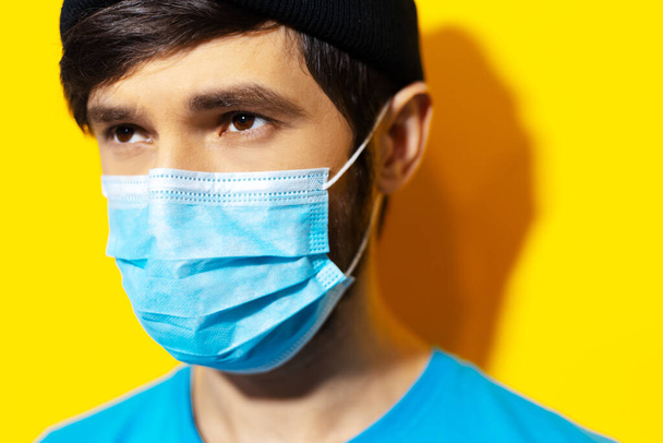 Studio close-up portrait of young guy wearing medical face mask against coronavirus on background of yellow color. Prevention of covid-19. - Foto, Bild