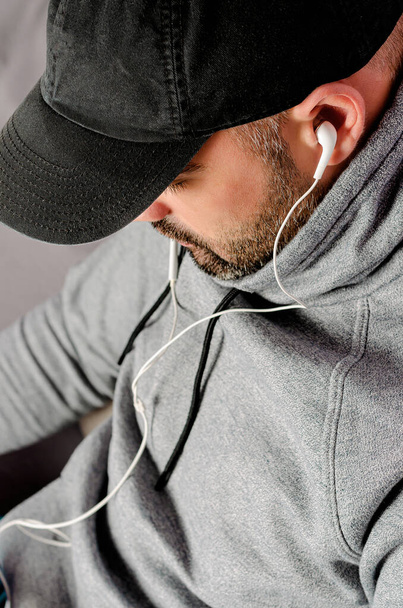 Gehakt portret van een man met baard in zwarte pet video 's kijken of naar de muziek luisteren met een oortelefoon. - Foto, afbeelding