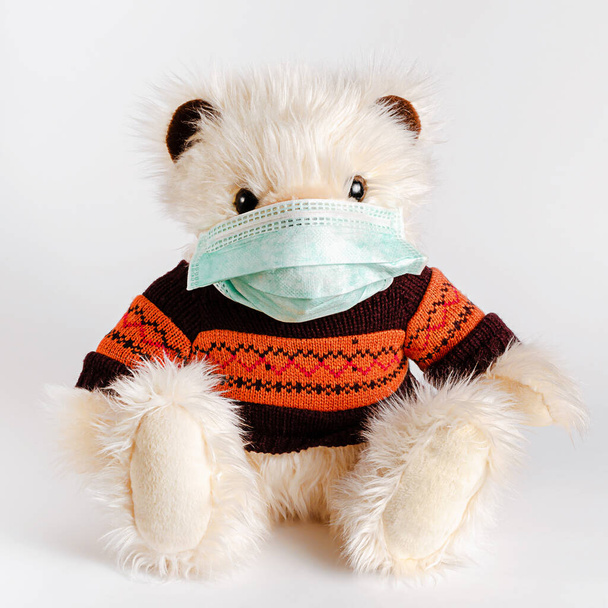 Teddy bear wearing sweater and protective medical mask. Pediatrics and disease prevention concept. - Photo, Image