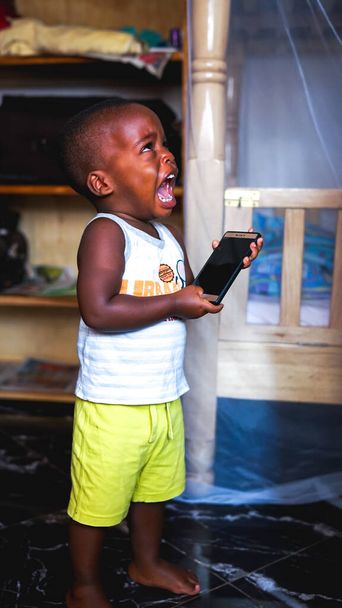 Kampala, Uganda - July 01, 2017: little African boy cries because the mother doesn't allow to play phone games very long, small children's tantrum, a difficult spoiled baby boy with gadgets addiction - Φωτογραφία, εικόνα