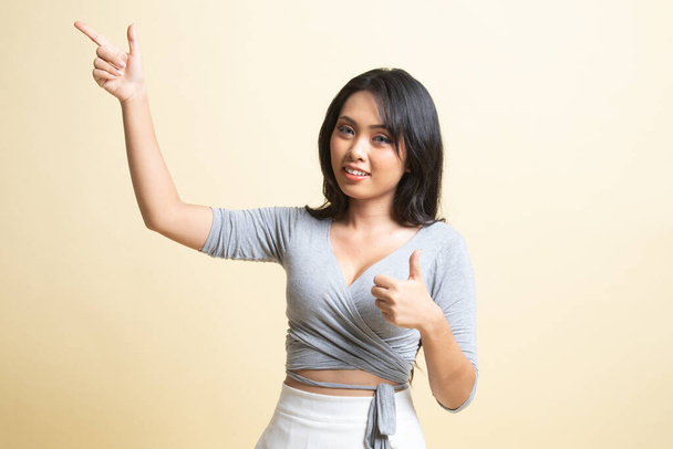 Young Asian woman point and thumbs up   on beige background - Zdjęcie, obraz
