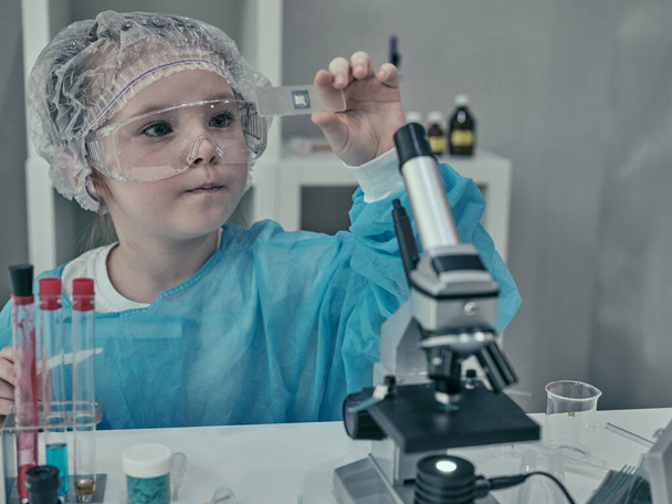 Pieni tyttö tekee tieteellisiä kokeita kemiallisilla ja biologisilla tuotteilla kotilaboratoriossaan. - Valokuva, kuva
