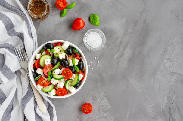 Görög saláta friss, lédús zöldségekből, feta sajtból, gyógynövényekből és olajbogyókból egy fehér tálban, sötét beton alapon. Egészséges étel. Vízszintes tájolás. Felülnézet, másolás - Fotó, kép