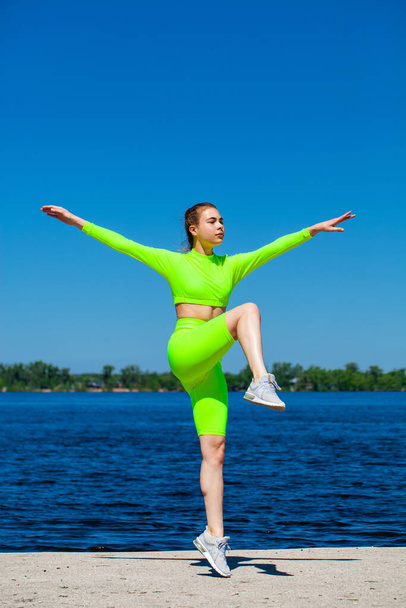 Full body portrait of a young athletic woman does physical exercises on the banks of the Volga River - Fotografie, Obrázek