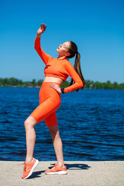 Full body portrait of a young athletic woman does physical exercises on the banks of the Volga River - Foto, afbeelding