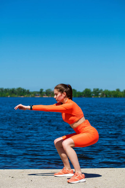 Outdoor Fitness - Exercises for the legs and buttocks. Young beautiful athlete is training on the banks of the Volga River - Fotó, kép