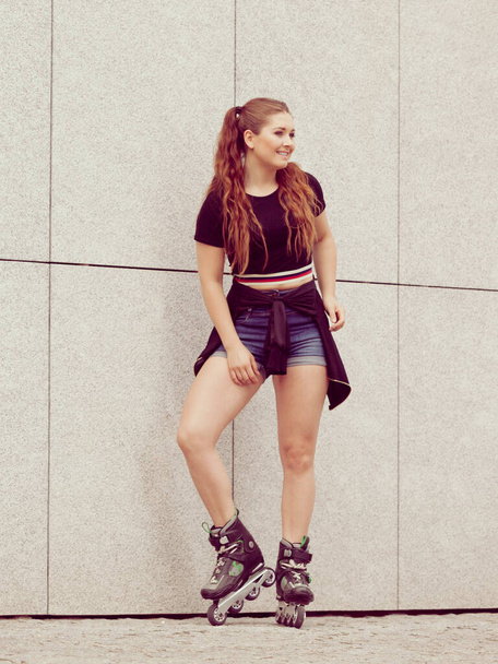 Молодая женщина в роликовых коньках стоит у бетонной стены в городе. Женщины - спортивные и веселые в летнее время. - Фото, изображение