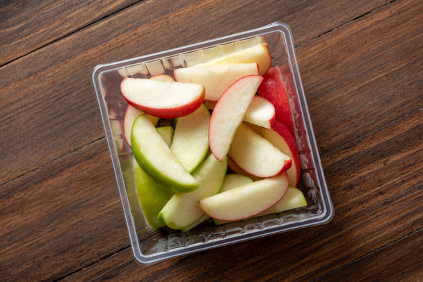 green and red apples are cut into pieces and placed in a clear box ready to be eaten , food delivery concept - Foto, Imagen