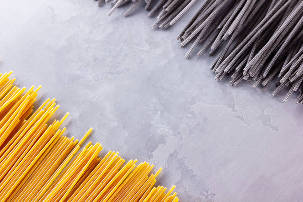 Black and yellow pasta on a gray background. Yellow and black spaghetti on cement background. Raw spaghetti bolognese. Food background concept. Top view - Φωτογραφία, εικόνα