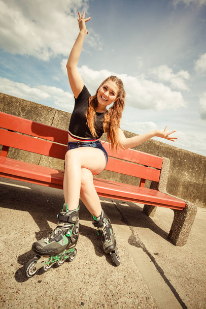 Happy joyful young woman wearing roller skates sitting on bench enjoying herself. Female being sporty having fun during summer time. - Photo, image