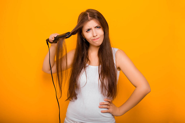 A young woman straightens her hair with a hair straightener. Damage to hair caused by a hot hair straightener. - Foto, immagini