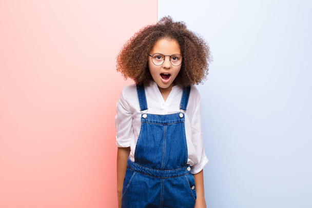african american little girl looking shocked, angry, annoyed or disappointed, open mouthed and furious against flat wall - Photo, image