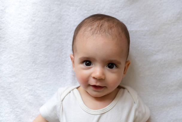 新生児。白い服を着た小さな男の子。幼児の美しい肖像画。大きな瞳の赤ちゃん. - 写真・画像
