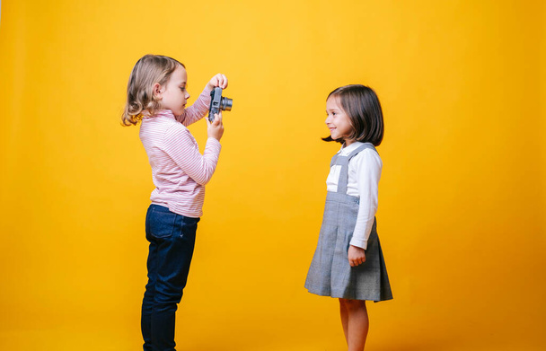 Δύο κορίτσια με φωτογραφική μηχανή σε κίτρινο φόντο - Φωτογραφία, εικόνα