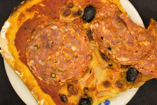 levensecht beeld van een zelfgemaakte pizza met pittige salami, zwarte olijven, tomaten en mozzarella - Foto, afbeelding