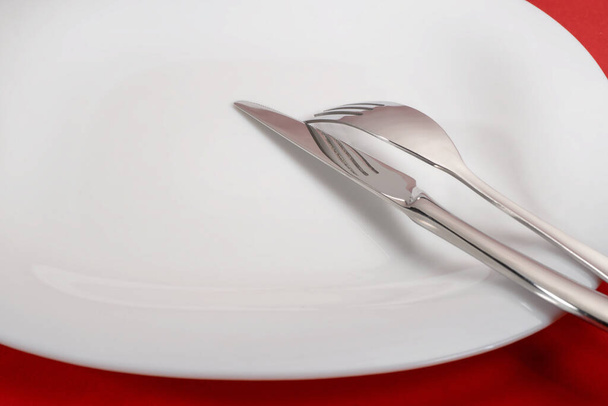 Fork and knife on white plate. On red table, selective focus - Foto, Bild