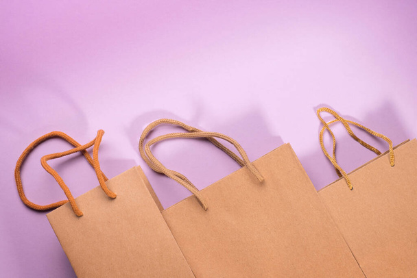 Craft cardboard gift bags with rope handles on violet background. Abstract shopping and gift theme composition and template - Φωτογραφία, εικόνα