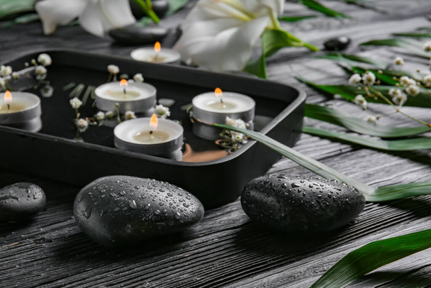 Spa stones and plate with water and candles on dark wooden background. Zen concept - Foto, Imagem