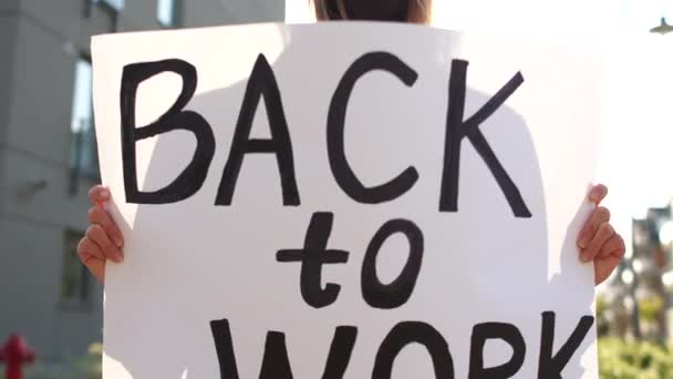 Zbliżenie kobiety w czarnej tarczy, trzymającej plakat z powrotem do pracy. Masowe protesty przeciwko środkom ograniczającym podczas kwarantanny Coronavirus covid-19 - Materiał filmowy, wideo