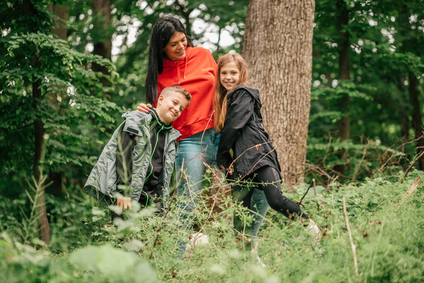 Hermosa madre joven y su hija e hijo caminando por el bosque. Familia feliz divirtiéndose juntos
. - Foto, Imagen