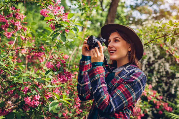 Woman photographer taking pictures using camera in summer garden shooting trees in blossom. Freelancer walking in park filming flowers blooming bushes. Hobby - Foto, imagen