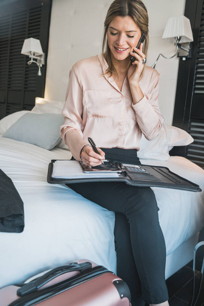 Portrait of young businesswoman talking on the phone at the hotel room. Business travel concept. - Photo, image