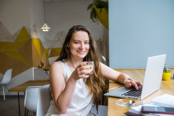 Portrait of smiling young business woman with coffee having a video call using laptop and headset sitting in cafe, coworking. Remote work, social networks, blogging. Telecommuting concept. Freelancer. - Foto, Bild