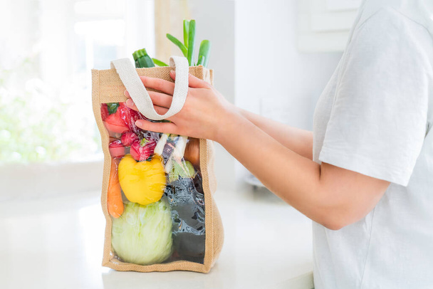 Close up female hands holding reusable bio eco sackcloth fabric bag packaging with fresh organic vegetables on white kitchen table. Home delivery concept. Local farmer healthy food. Zero waste. - Фото, зображення