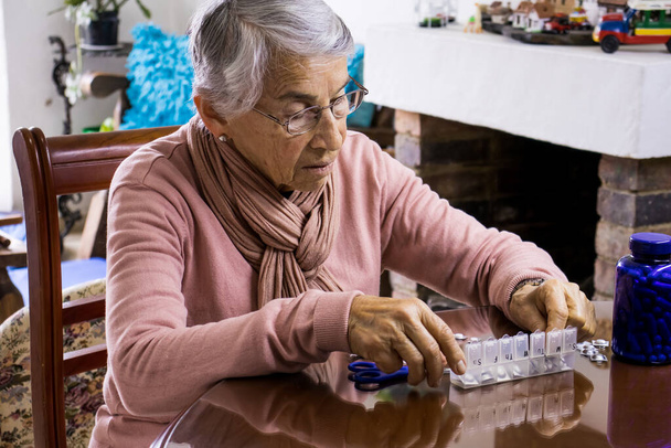 Donna anziana a casa organizzare i suoi farmaci di prescrizione in un organizzatore pillola settimanale
 - Foto, immagini