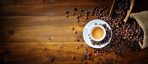 Kubek espresso i ziarna kawy z miarką i workiem jutowym na drewnianym tle, widok z góry, miejsce na tekst. - Zdjęcie, obraz