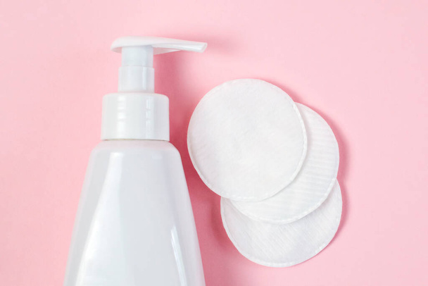 White bottle with gel for washing and wiping faces, soft cotton pads and sticks, micellar water for makeup removal, skin cleansing and cosmetic treatments on a pastel pink background with. - 写真・画像