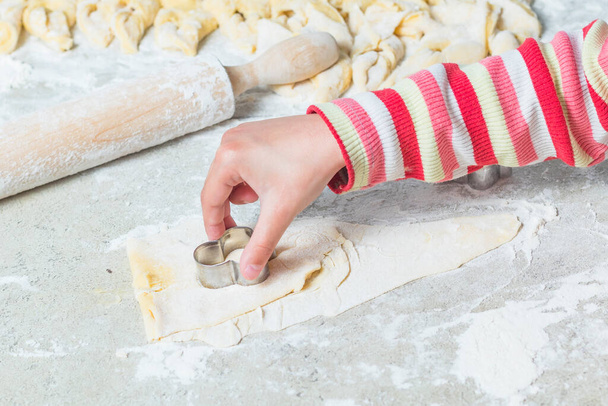 Home kitchen. On the table is a dough for baking. A child squeezes a form in it. - Photo, Image