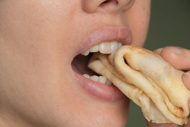 Το στόμα μιας κοπέλας δαγκώνει μια τηγανίτα από κοντά. - Φωτογραφία, εικόνα