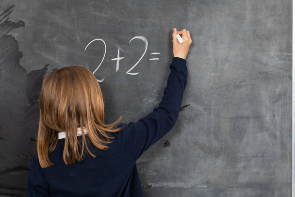 He writes on the chalkboard with chalk. Math problem. A girl at the chalkboard. - Photo, image
